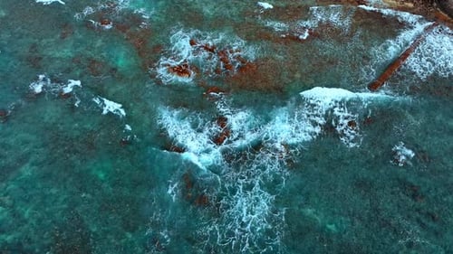 Turquoise waters of the Pacific Ocean. White foamy waves roll to the shore. Aerial view.