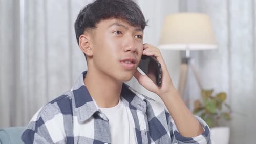 Close Up Of Asian Teen Boy Talking On Smartphone While Sitting On Sofa In The Living Room At Home