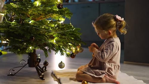 Little Girl Plays with Christmas Ornaments by Tree