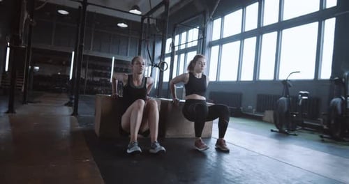Dos jóvenes y hermosas mujeres caucásicas atléticas haciendo ejercicio juntas en un gran gimnasio, entrenamiento con entrenador personal
