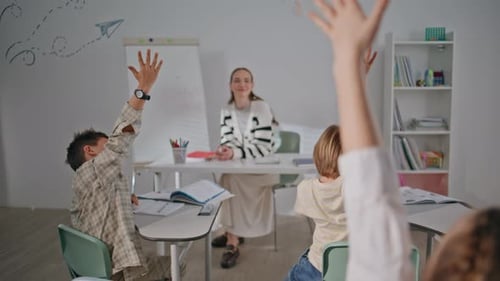 Raising Hands Kids Answering Lesson Sitting Desks in School Class Back View