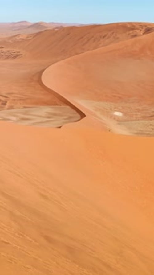 Aerial drone view along the ridge of a massive sand dune in the Namib Desert with smooth wind shaped
