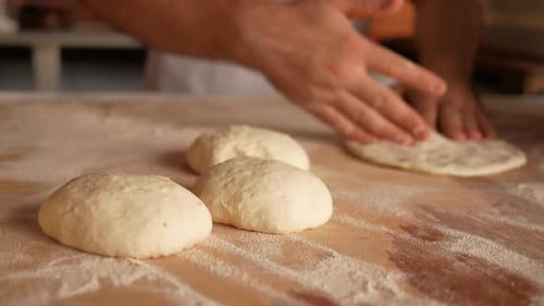 Hands Flattening Dough on a Floured Surface