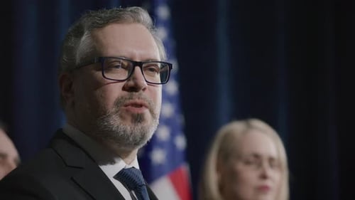Man speaks at press conference with flag