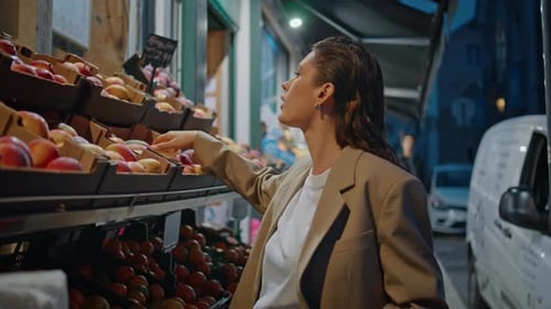 Jeune femme choisissant des fruits à l'épicerie de rue en fin de soirée, gros plan