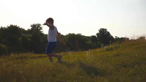 Young Boy with Raised Hands Running on Green Grass at the Field on Sunny Day