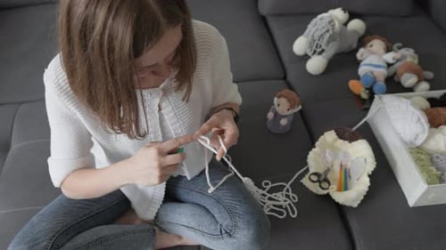 Woman Crocheting White Yarn on Gray Sofa