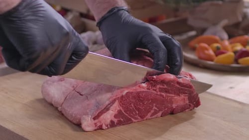 Gloved Hands Cutting Raw Beef Loin on Wood Board