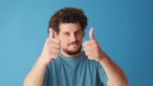 Close up, positive man showing double thumbs up gesture isolated on blue background in studio
