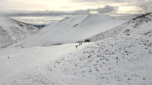 Drohnenfilmansicht auf eine Gruppe von Menschen auf Schneeschuhen, die einen verschneiten Berg erklimmen