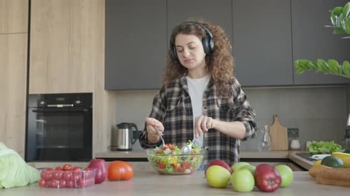 Woman Mixing Salad with Headphones in Kitchen