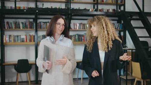 In the Modern Library Two Women are Deeply Engaged in Conversation Surrounded By Bookshelves and