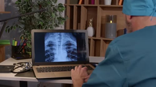 Mature Male Orthopedist with Laptop Checking Xray Image of Human Spine