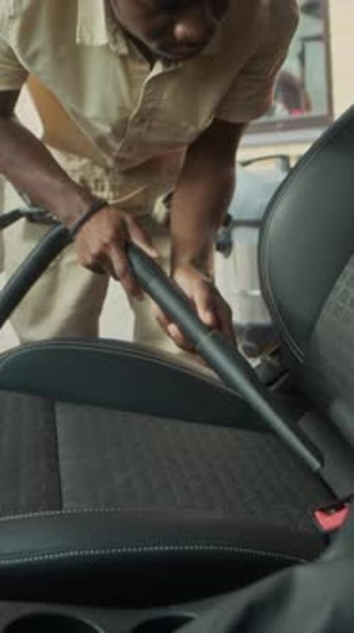 Vertical of Mechanic Cleaning Red Car Interior with Vacuum Hose in Garage