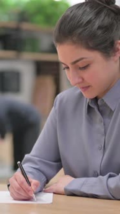 Focused Young Woman Writing on Paper at Desk