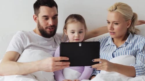 Smiling family relaxing in bed with tablet computer