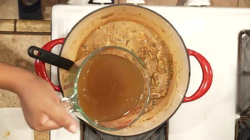 Adding vegetable stock broth to wild rice mushroom soup simmering on the stove - overhead view WILD