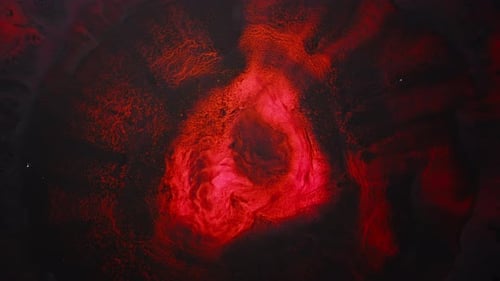 Red pigment mixing in liquid captured in view with abstract swirling energy