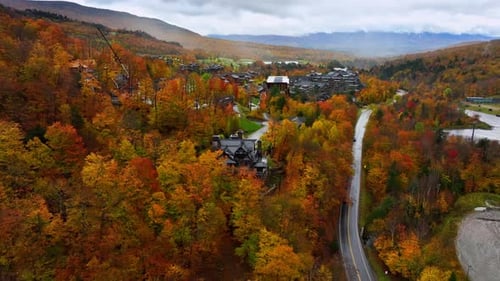 Flying closer to houses among red, yellow, orange trees. Drone footage above Vermont, New England