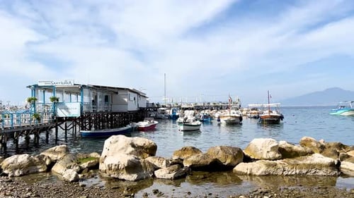 Eine Uferszene mit festgemachten Booten neben einem Pier mit Gebäuden, unter klarem Himmel und einem Berg