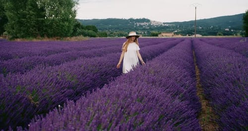 Young Woman in White Dress Walking Through a Lavender Field on Sunset