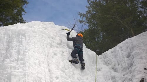 A climber reaches the summit of a frozen cliff face
