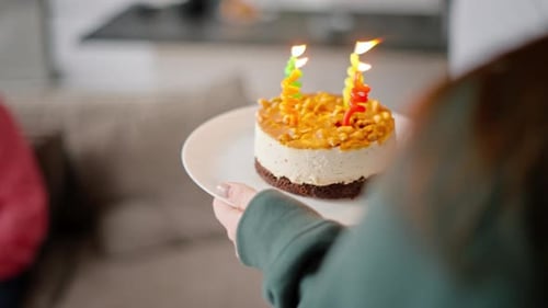 Over Her Shoulder a Brunette Girl in a Green Jacket Brings a Small Cake with Candles for Her Dad in