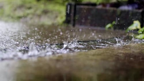 Wassertropfen, die in die Pfütze fallen, auf den Bürgersteig spritzen, aus nächster Nähe, langsamer Regen