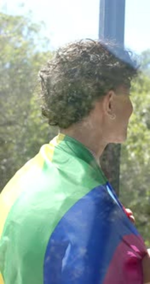 Young Adult with Pride Flag Standing By Window