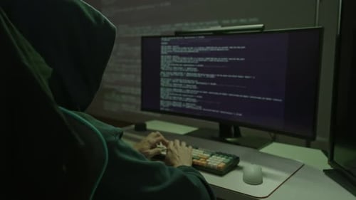 Un hacker cagoulé tapant sur le clavier de l'ordinateur dans une pièce noire se livrant à une violation de données sur la cybercriminalité