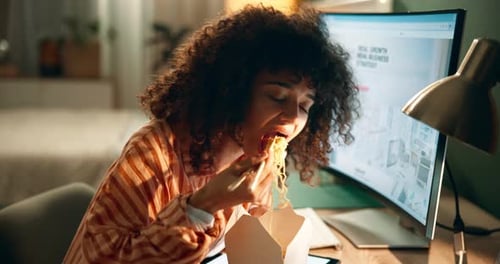 Woman Eating Noodles at Desk While Using Computer