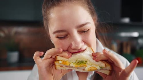 Young Woman Enjoying Sandwich for Breakfast Indoors