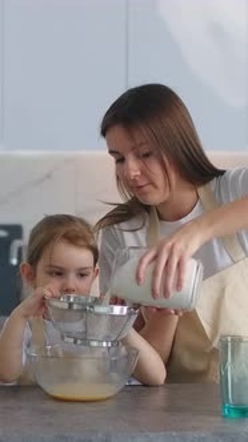 Mother and Daughter in Matching Aprons Sifting Flour Together in a Bright Modern Kitchen While