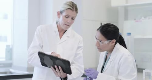 Two female scientists analyzing data on digital tablet