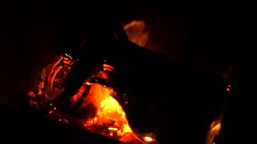 Home log wood fire burning in slow motion with bright hot embers, ash and orange red flickering flam