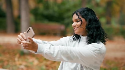 Young Indian Woman Taking Selfie Video with Smartphone in Autumn Park