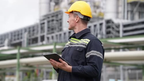 Ingénieur de sexe masculin en équipement de sécurité vérifiant sur une tablette numérique travaillant dans une raffinerie de pétrole