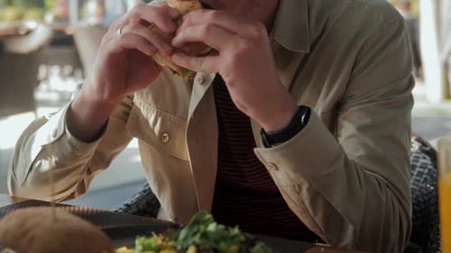 A Man Eats a Chicken Sandwich Sitting in a Cafe in the Fresh Air