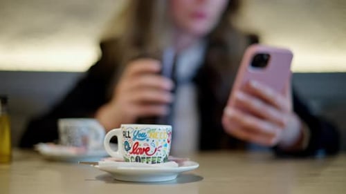 A cup of coffee at a cafe with a woman scrolling on her phone on the background