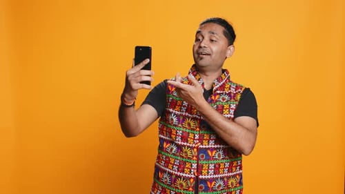 Joyous Man Greeting Friend Over Online Videocall on Cellphone Studio Background