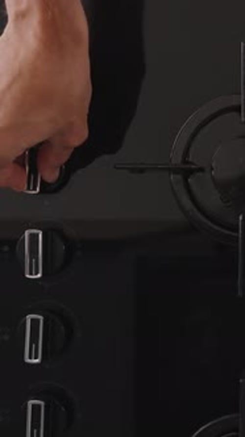 Vertical video. A black glass gas stove with four burners. I turn the knob and ignite one of them.