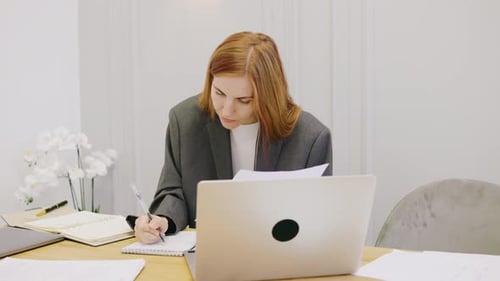 A Dedicated Professional Redhaired Businesswoman is Focused While Working at Their Modern Desk Which