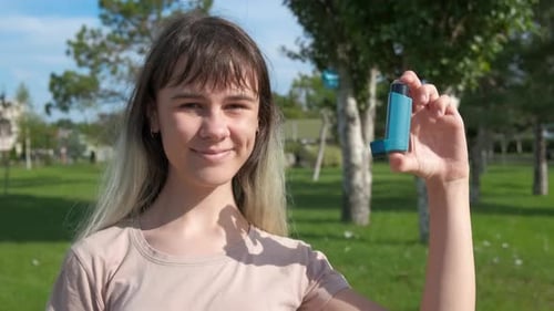 Young Adult Holding Blue Asthma Inhaler in Park