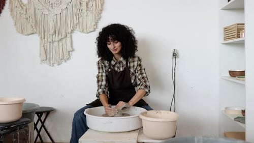 Female Potter Crafting Ceramic Bowl at Pottery Wheel in Studio