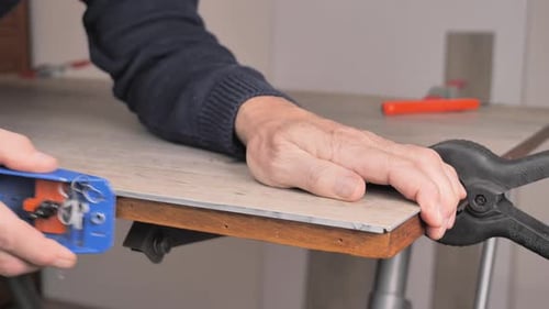 Detalhe das mãos de um homem aplainando pisos de vinil no tamanho desejado enquanto faz biscates em sua casa