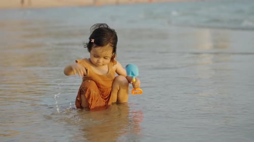 happy toddler baby girl playing toy and water on the sea beach