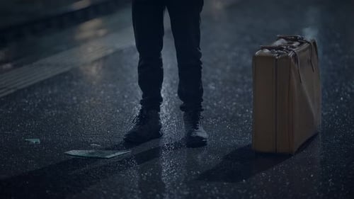 A Traveler in the Rainy Night Holds a Suitcase Amidst the City Ambiance with a Lonely Moody Feel