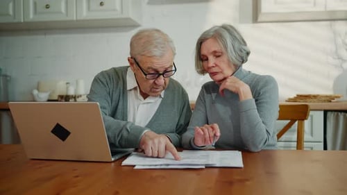 Senior Couple Reviewing Finances Together at Wooden Kitchen Table