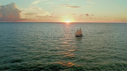 Sailboat silhouetted against ocean sunset on open horizon