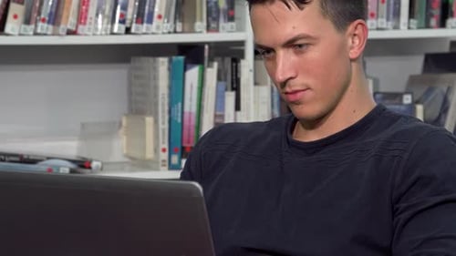 Focused Male Student Immersed in Laptop Work at a Vibrant Campus Library